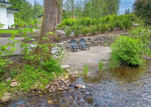 Un patio de piedra con sillas Adirondack, un arroyo pequeño y follaje circundante.