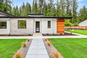 Una casa moderna con fachada de piedra, una extensión de madera y un césped bien cuidado.