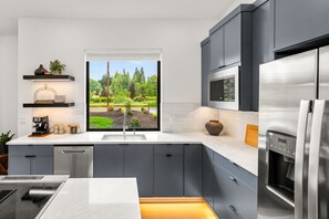 Una cocina moderna con un ventanal grande, electrodomésticos integrados y vistas a un jardín.
