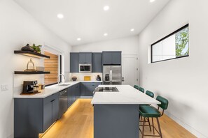 Una cocina moderna con gabinetes grises, una isla central y una zona de comedor con sillas verdes.