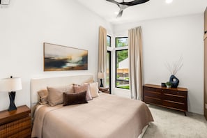 Un dormitorio con cama, mesitas de noche, cómoda, un cuadro y una ventana con cortinas.