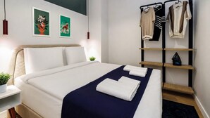 A modern hotel room with a neatly made bed, a bedside table with a plant, a wall-mounted shelf with clothes, and two framed artworks. - Glamorous Cihangir 3 Bedrooms Apt At Monnas Suite (Istanbul)