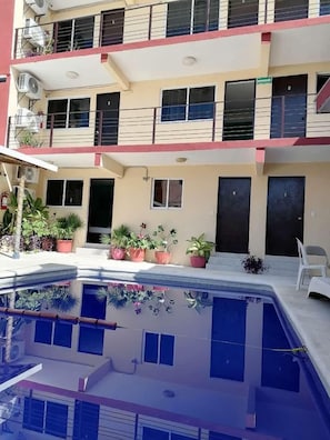 Um edifício com vários andares, varandas, plantas em vasos e uma piscina.