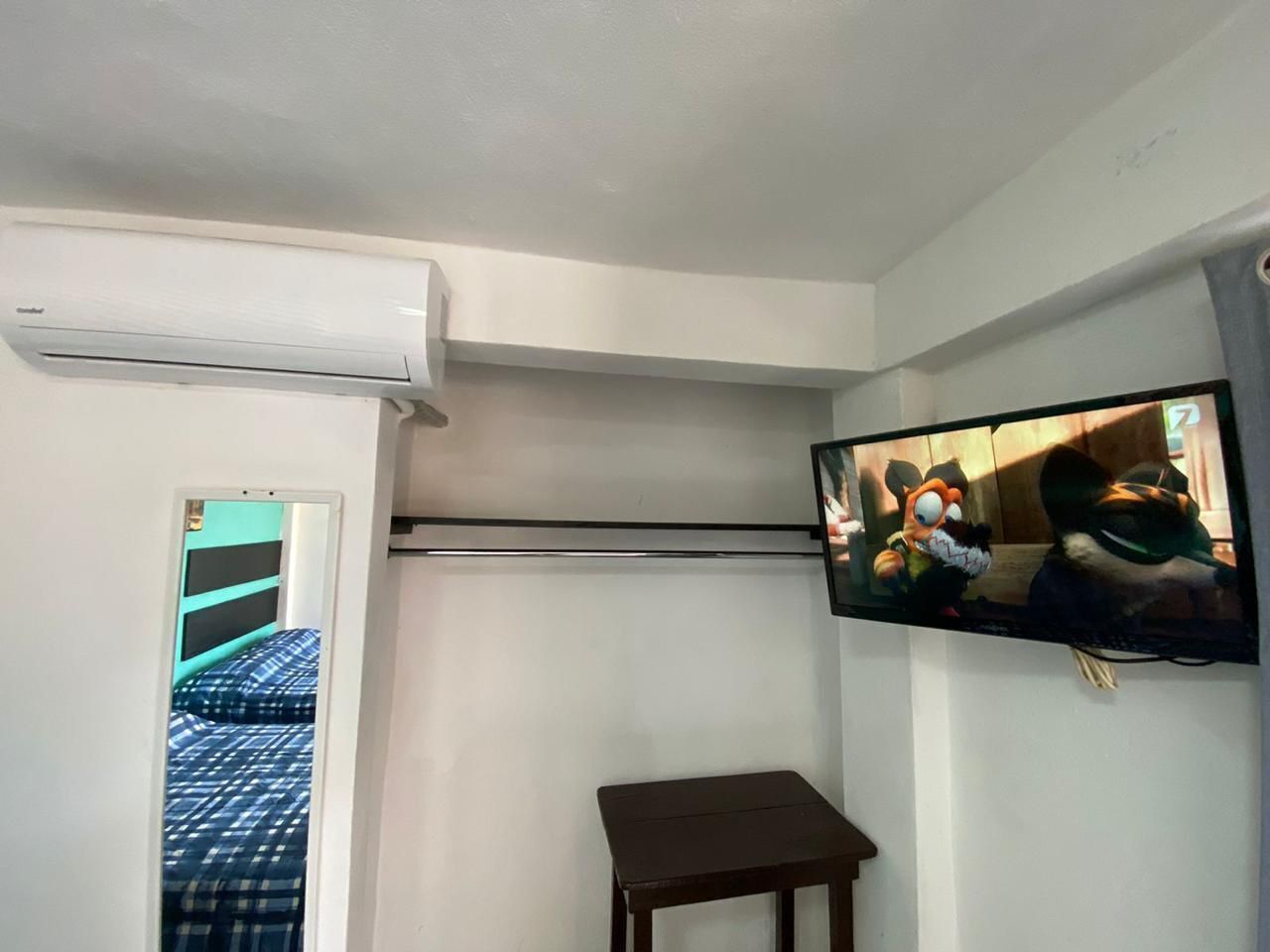 A room with a bed, a small table, an air conditioning unit, and a wall-mounted television.