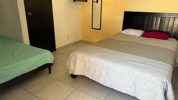Una habitación con dos camas, una con cubrecama verde y la otra con cubrecama blanca y almohada roja.