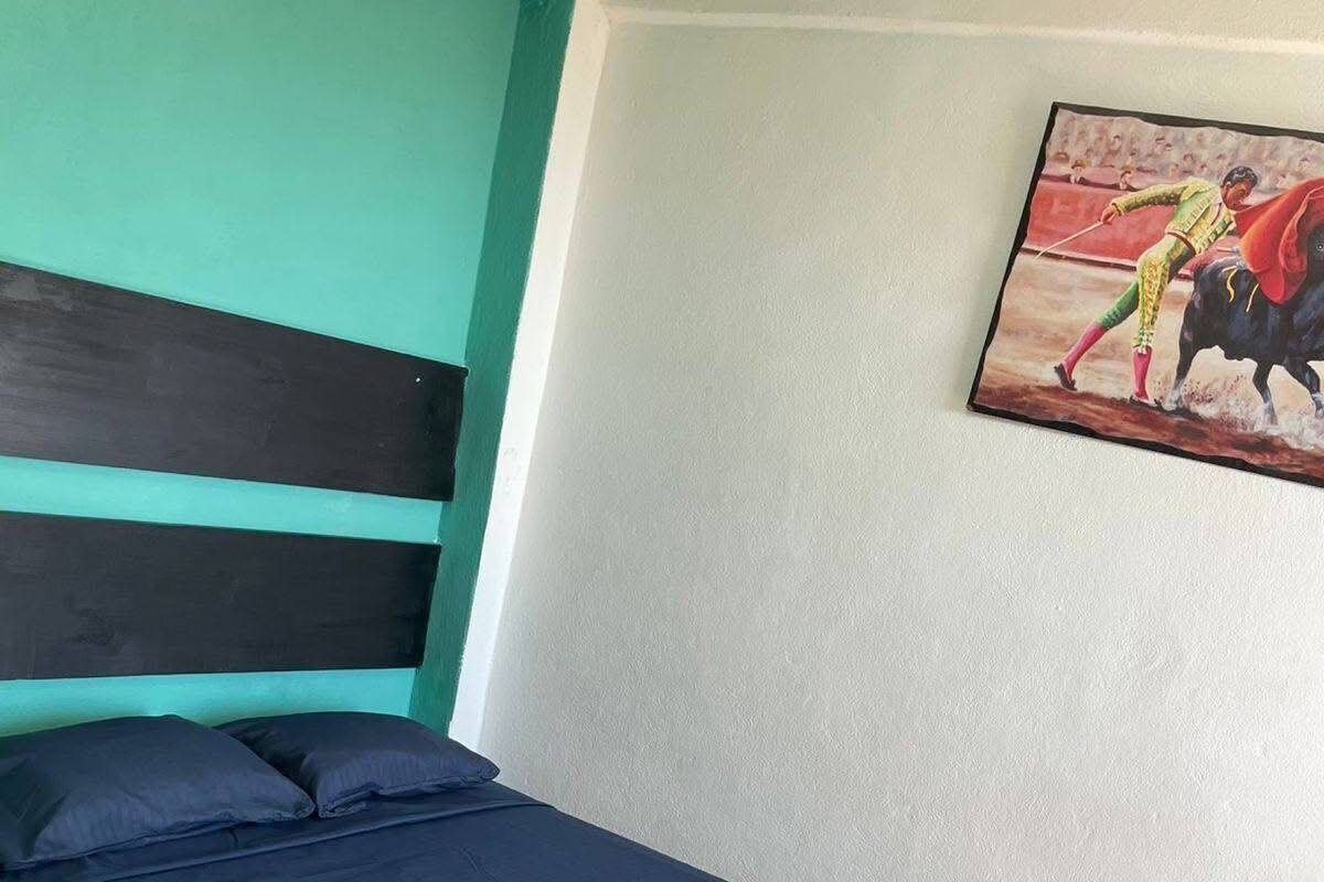 A bed with a blue and red bedspread, a teal wall, and a painting of a bullfighter.