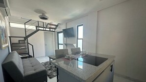 A modern kitchen with a central island, a dining area with a sofa, and a staircase leading to an upper level. - Dog-friendly Loft With Rooftop Infinity Pool, Gym, Balcony & Central AC (Cabo San Lucas)