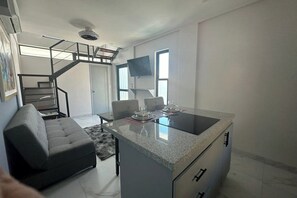 Eine moderne Küche mit einer zentralen Kochinsel, ein Essbereich mit einer Couch und eine Treppe, die zu einer oberen Ebene führt.