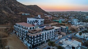 A multi-story hotel with a modern architectural design, located in a hilly area with a view of the cityscape. - Dog-friendly Loft With Rooftop Infinity Pool, Gym, Balcony & Central AC (Cabo San Lucas)