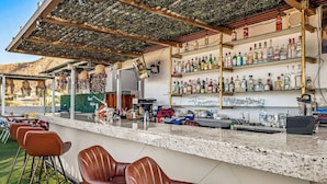 A bar area with a counter, bar stools, shelves with bottles, and a view of the outdoors. - Dog-friendly Loft With Rooftop Infinity Pool, Gym, Balcony & Central AC (Cabo San Lucas)