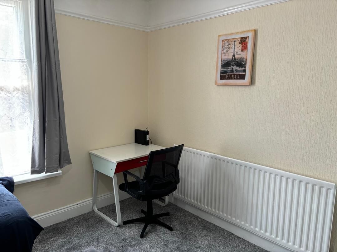 Een kleine kamer met een bureau, stoel, radiator en een poster aan de muur.