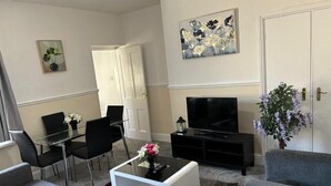 Una sala de estar moderna con televisor de pantalla plana, una mesa de comedor con sillas, un sofá y una mesa de centro.