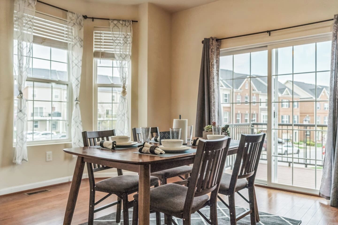 A dining area with a round table, six chairs, and a view of buildings through large windows.