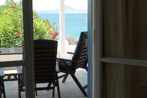 An open door leading to a balcony with a table and chairs, overlooking a body of water and greenery. - Charming Naxos Villa, Ocean Views, Modern Comfort, Tranquil Escape (Naxos)