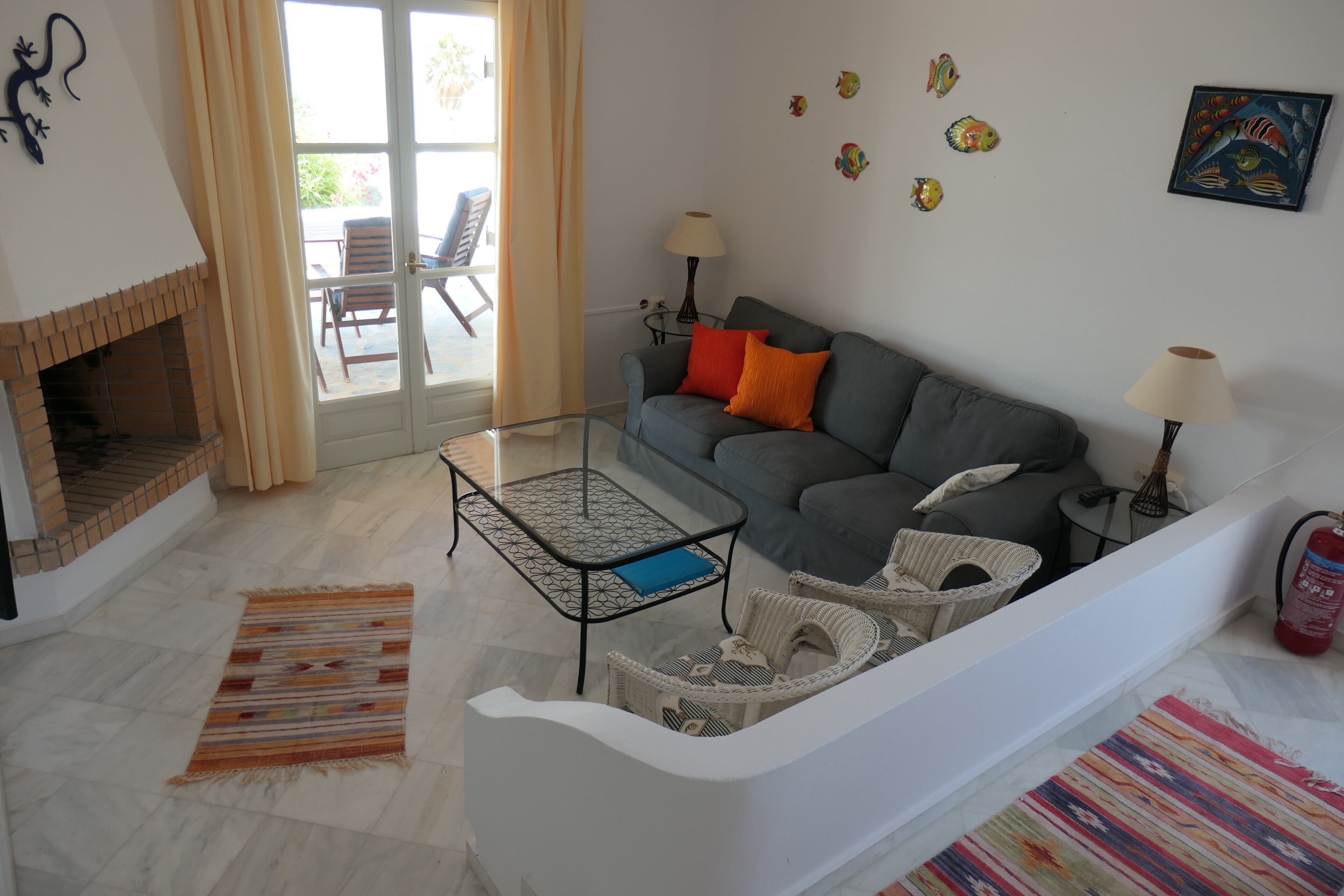 Ein Wohnzimmer mit einer Couch, zwei Beistelltischen, einem Glastisch, einem Kamin, einem Teppich mit Muster und einer Wand mit Fischmotiven.