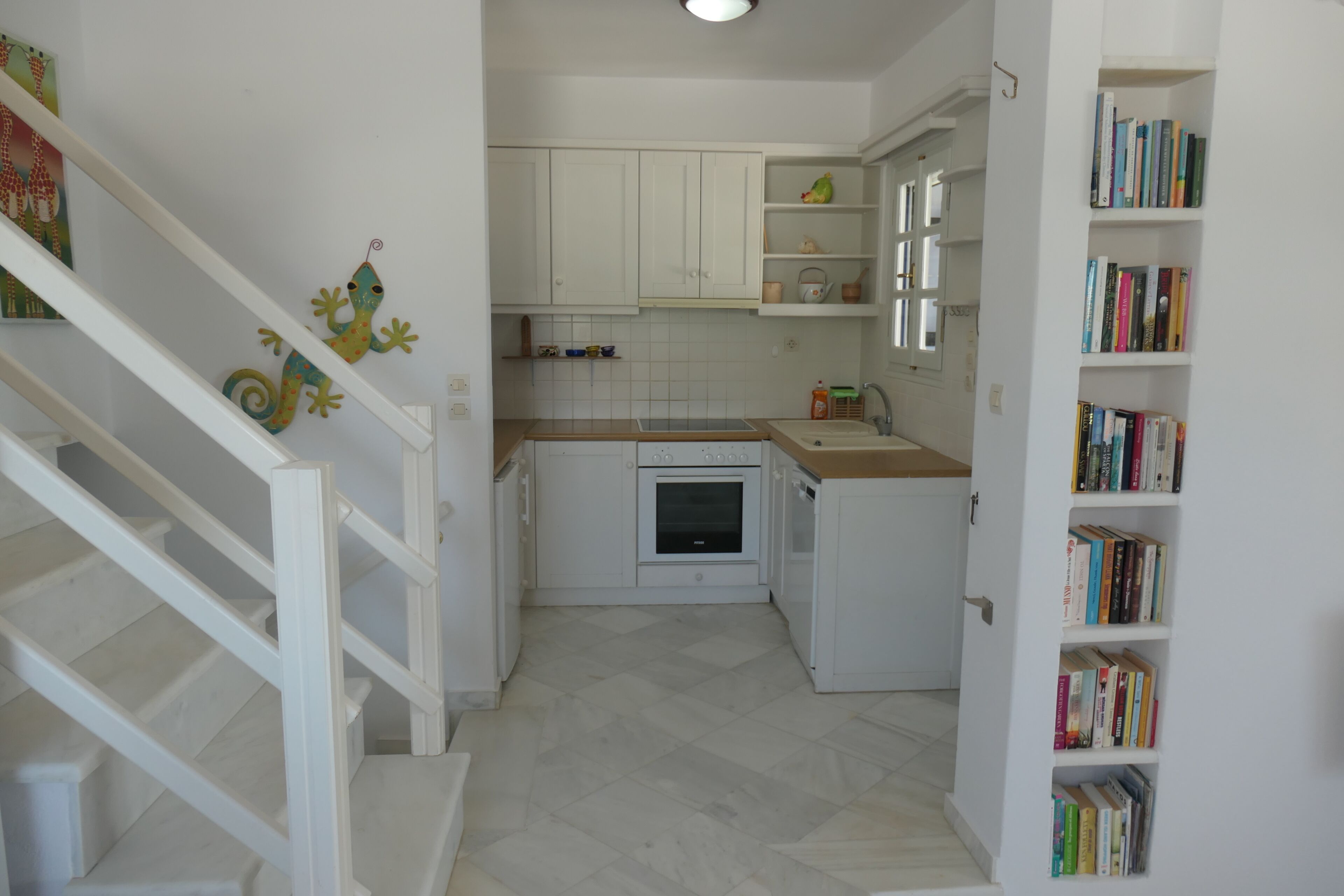 A kitchen with white cabinets, a built-in oven, and a bookshelf filled with books.