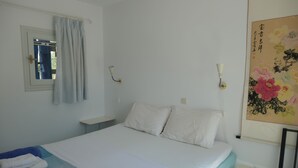 Ett hotellrum med en säng, ett sängbord, en vägglampa och en tavla.