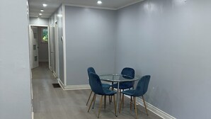 Huoneessa on pyöreä lasipöytä ja neljä sinistä tuolia, kuviollinen matto sekä käytävä, jossa on ovi toiseen huoneeseen.