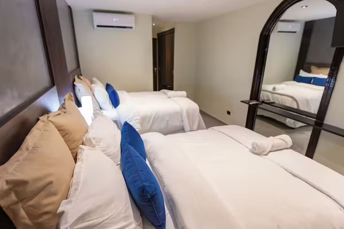 A hotel room with two beds, a mirror, and an air conditioning unit.