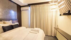 A hotel room with a large bed, a headboard, a wall-mounted air conditioning unit, a curtain, and a modern light fixture. - Boutique Hotel - Suite Sencilla Ramada (San Salvador)