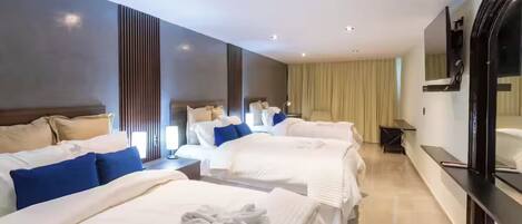A hotel room with three beds, a TV, a mirror, and a bedside table.