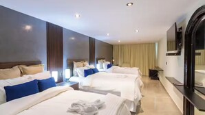A hotel room with three beds, a TV, a mirror, and a bedside table.
