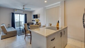 A modern living room with a sofa, a dining table, and a kitchen island. - Dog-friendly Apartment With Rooftop Infinity Pool, Gym, Central AC & Balcony (Cabo San Lucas)