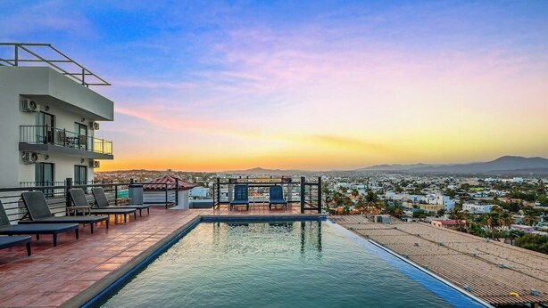 A rooftop pool with lounge chairs, a view of the cityscape, and a sunset. - Dog-friendly Apartment With Rooftop Infinity Pool, Gym, Central AC & Balcony (Cabo San Lucas)