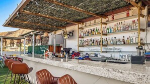 An outdoor bar area with a counter, bar stools, and shelves stocked with bottles. - Dog-friendly Apartment With Rooftop Infinity Pool, Gym, Central AC & Balcony (Cabo San Lucas)
