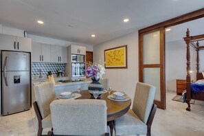 A modern kitchen with a dining area, a bed with a wooden headboard, and a large painting on the wall. - Dog-friendly Apartment With Rooftop Infinity Pool, Gym, Central AC & Balcony (Cabo San Lucas)