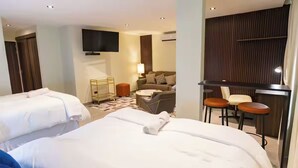 Ett hotellrum med två sängar, en soffa, en TV och ett skrivbord med stolar.