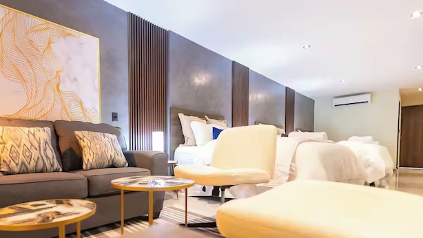 A modern hotel room with a sofa, armchair, and a bed with white linens.