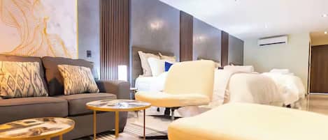A modern hotel room with a sofa, armchair, and a bed with white linens.