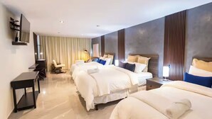 A hotel room with three beds, a desk, a chair, and a TV.
