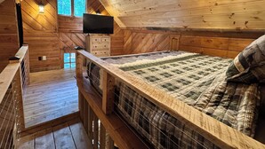 A wooden cabin bedroom with a bed, a TV, a window, and a wooden ceiling.