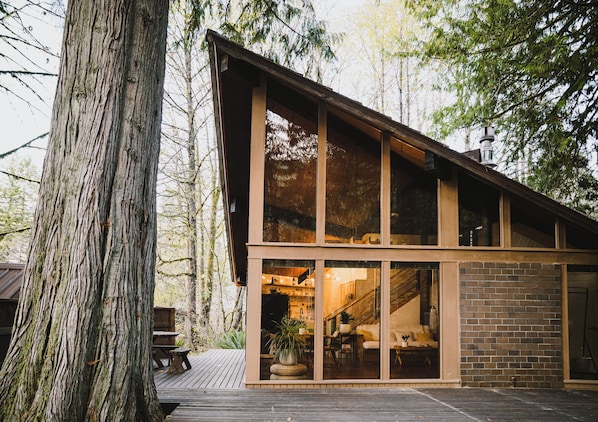 A modern wooden cabin with large windows, a deck, and a staircase leading to the upper level.