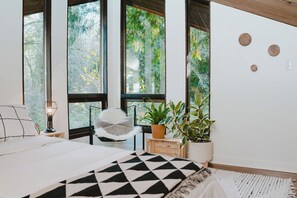 A bedroom with a bed, a chair, a lamp, and potted plants.