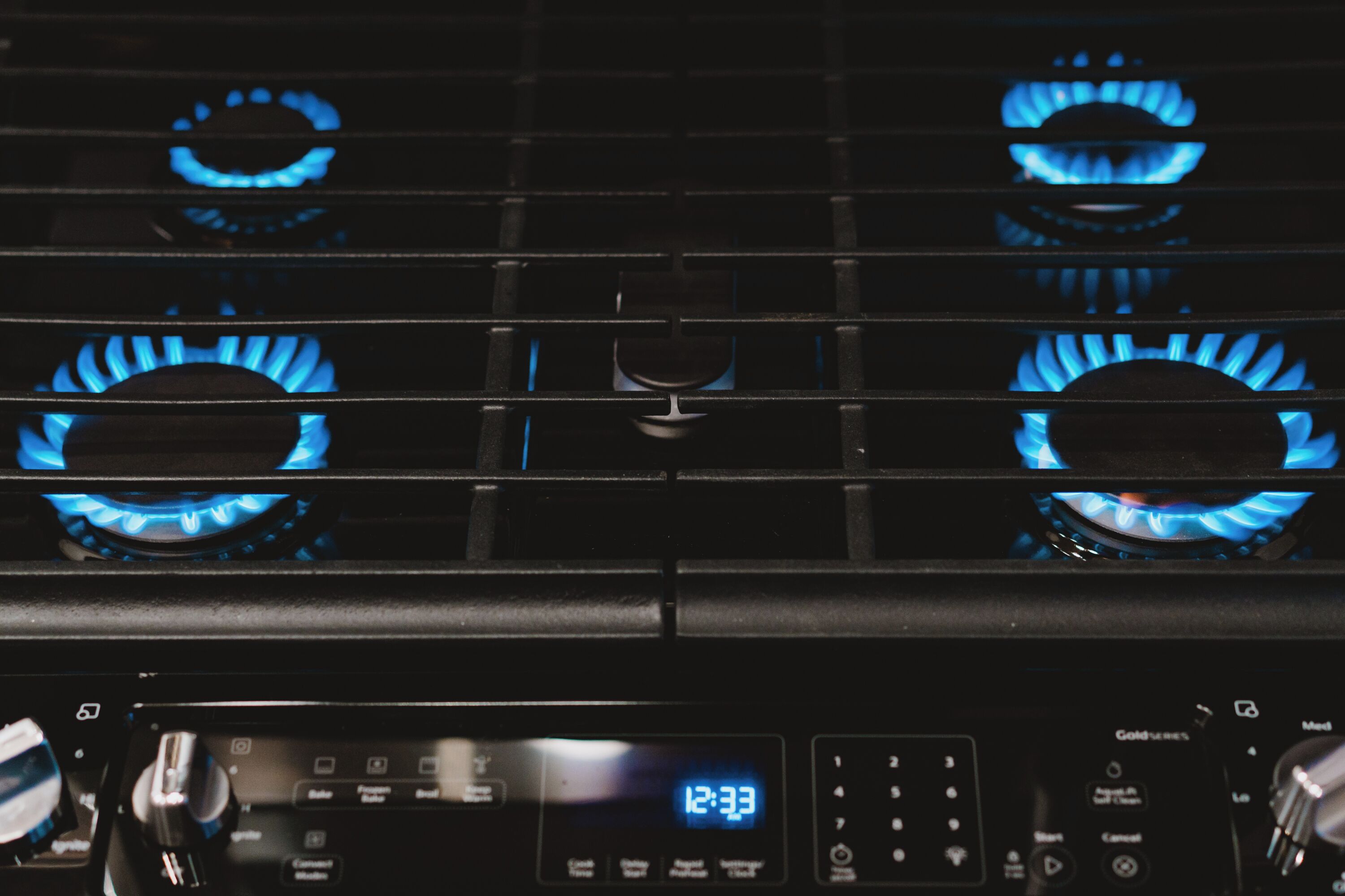 A kitchen with four blue gas burners and a digital clock displaying 12:33.