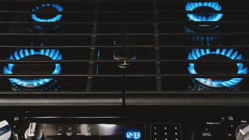 A kitchen with four blue gas burners and a digital clock displaying 12:33.