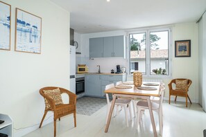 Eine moderne Küche mit hellblauen Schränken, einem Esstisch mit weißen Stühlen, Korbstühlen und Blick durch große Fenster.