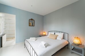 Ein Schlafzimmer mit einem Bett, zwei Nachttischlampen, einem Spiegel und einem Badezimmer mit Dusche und Toilette.