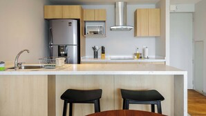 A modern kitchen with a central island, stainless steel appliances, wooden cabinets, and black bar stools. - w* | Upscale 1BR w/ AC in the Heart of Roma Sur (Ciudad de México)