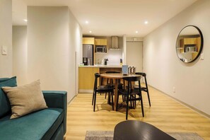 Ein gemütlicher Wohnbereich mit Sofa, Esstisch, St ühlen, Küchenzeile mit Geräten und einem runden Spiegel an der Wand.
