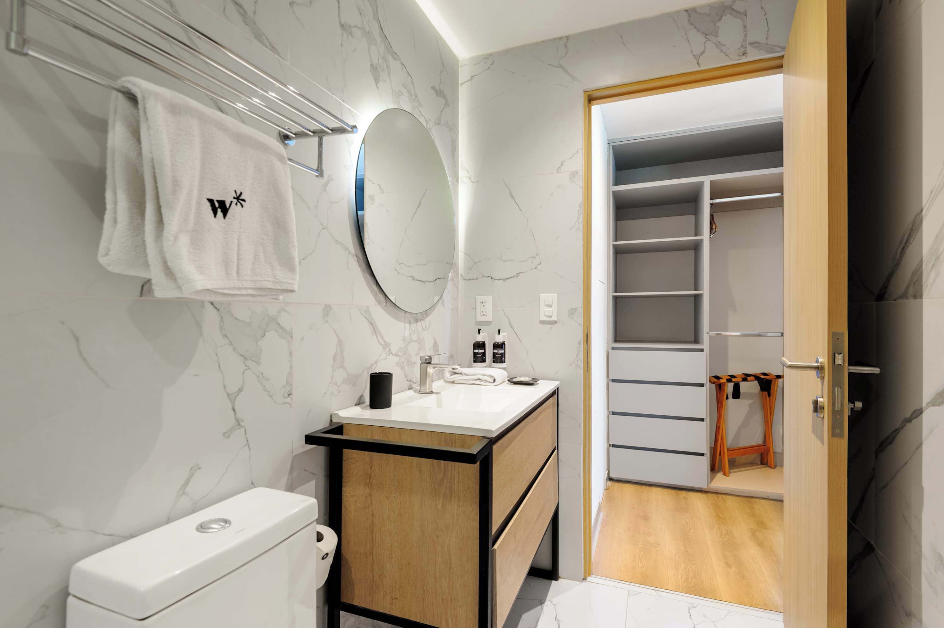 Ein modernes Badezimmer mit Marmorverkleidung, einer Toilette, einem Waschbecken mit Spiegel und einem begehbaren Kleiderschrank.