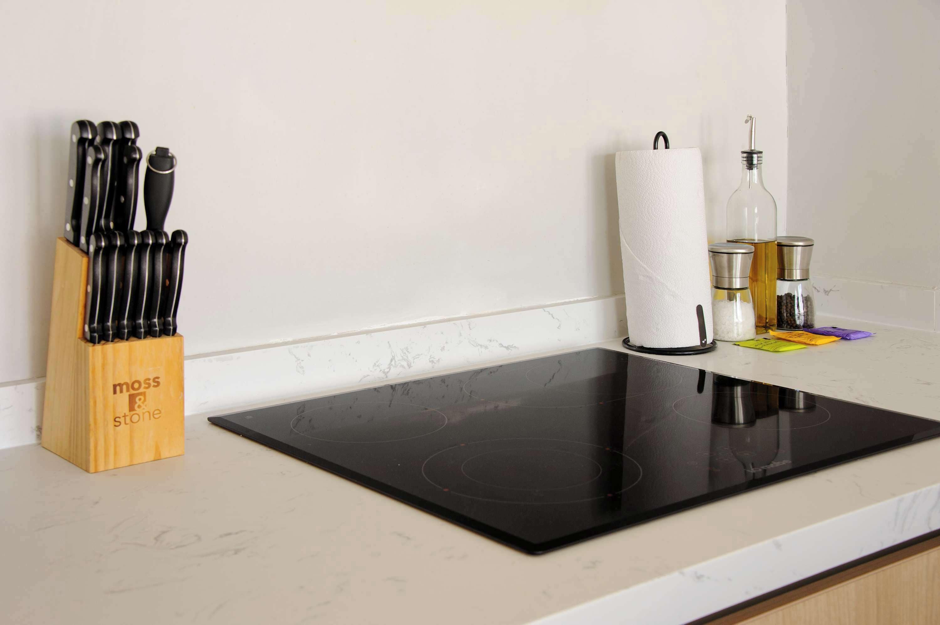 Une cuisine équipée d’une plaque de cuisson à induction noire, d’un bloc à couteaux, d’un rouleau d’essuie-tout et d’une bouteille d’huile.