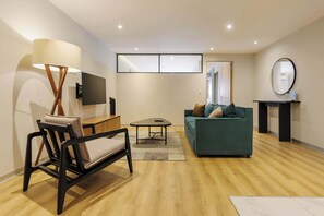 Ein modernes Wohnzimmer mit einer Couch, einem Sessel, einem Couchtisch, einem an der Wand befestigten Fernseher und einem Wandspiegel.