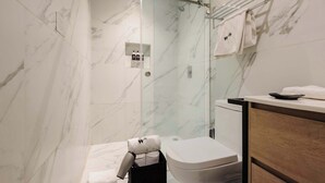Um banheiro moderno com chuveiro em gabinete de vidro, paredes de mármore, vaso sanitário branco e toucador de madeira.