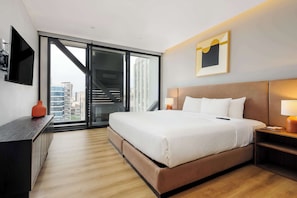 Ein modernes Hotelzimmer mit einem großen Bett, einem Schreibtisch, einem Fernseher und Blick auf die Stadt durch ein großes Fenster.
