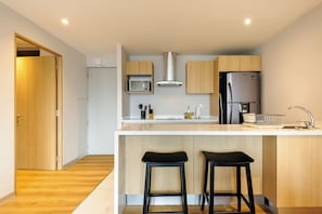 A modern kitchen with a central island, wooden cabinets, a stainless steel refrigerator, and two black bar stools. - w* | Amazing 1BR w/ AC in the Heart of Roma Sur (Ciudad de México)