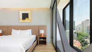 A hotel room with a bed, bedside table, lamp, and a city view through large windows. - w* | Stunning 1BR w/ AC in the Heart of Roma Sur (Ciudad de México)